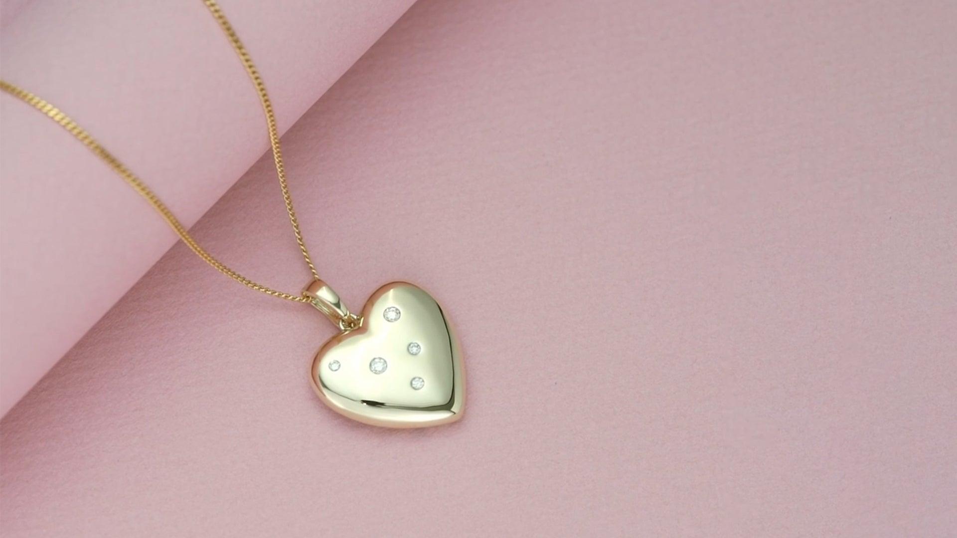 flatlay image of a golden heart pendant necklace with bezeled diamond gemstones