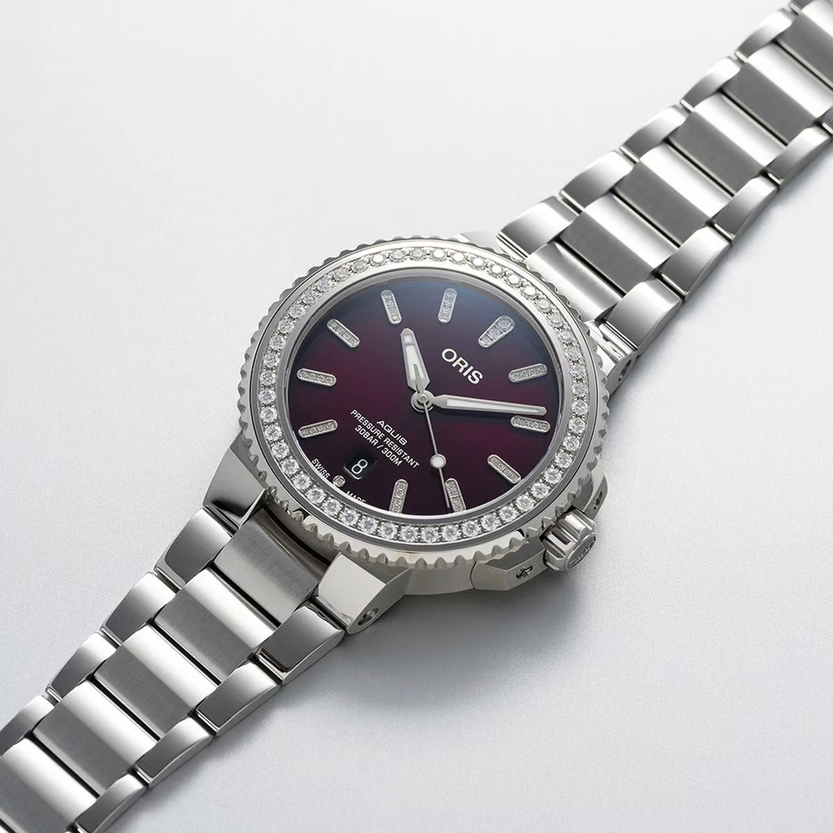 Three-quarter angle view of the Oris Aquis Date Relief 41.50cmm Automatic Watch 733 7766 4998MB, highlighting the diamond-set case and domed sapphire crystal. The red dial and date window are visible from this angle.