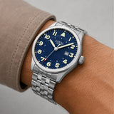 The Loyal Adventurer Pilot Watch worn on the wrist, showing the true scale of the 40mm case and blue dial. The stainless steel finish and 12 o'clock orientation triangle give this quartz watch a distinctive, versatile look for daily wear, alongside the bonus blue leather strap included with this set.