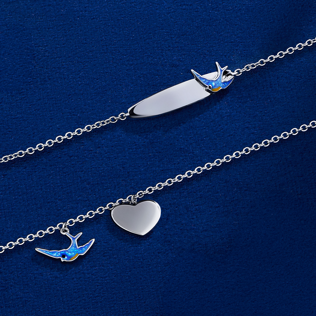 The Wallace Bishop Bluebird of Happiness Heart Bracelet in Sterling Silver for children, reference 32BLBB01, measuring 160mm in length, shown together with the Bluebird of Happiness ID Plate Bracelet in Sterling Silver, reference 32BTBB01, on a 160mm cable chain. The heart bracelet features a blue enamel bluebird and a polished silver heart as solid charms, and the ID plate bracelet features a 5mm engravable plate with a bluebird detail in blue enamel.
