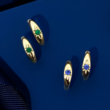 Front-on view of two pairs of Wallace Bishop Starburst Huggies in 9ct Yellow Gold, each measuring 14.50mm in length: the Created Emerald Starburst Huggies, reference 34ERSBEY, and the Created Sapphire Starburst Huggies, reference 34ERSBSY. Each huggie holds a 2.5mm round created gemstone, green emerald or blue sapphire, in a star hammer setting.