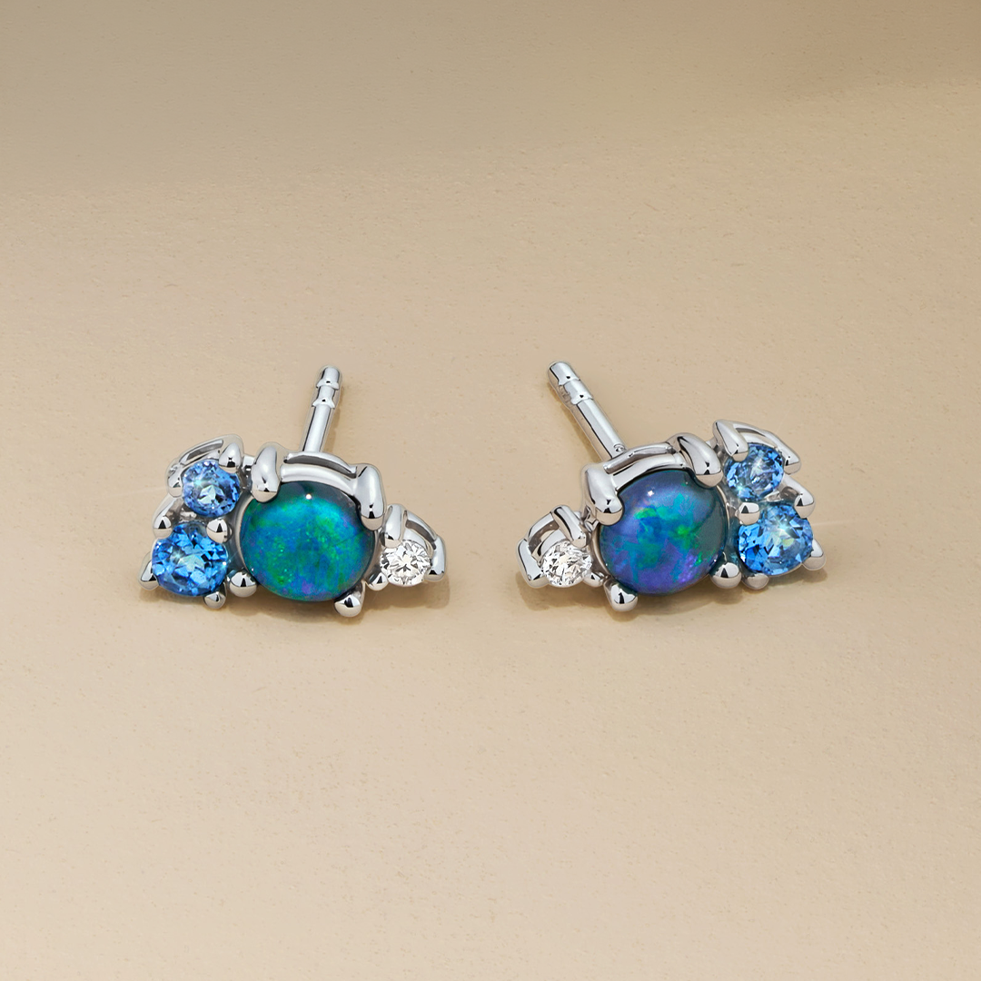 Flat lay view of the Wallace Bishop Triplet Opal, Swiss Blue Topaz, London Blue Topaz & Lab-Grown-Diamond Cluster Stud Earrings in Sterling Silver, reference 36ERCLUSS, laid flat with butterfly backs. Each stud features a 4mm round triplet opal in a claw set cluster with two blue topaz and a small lab-grown diamond.