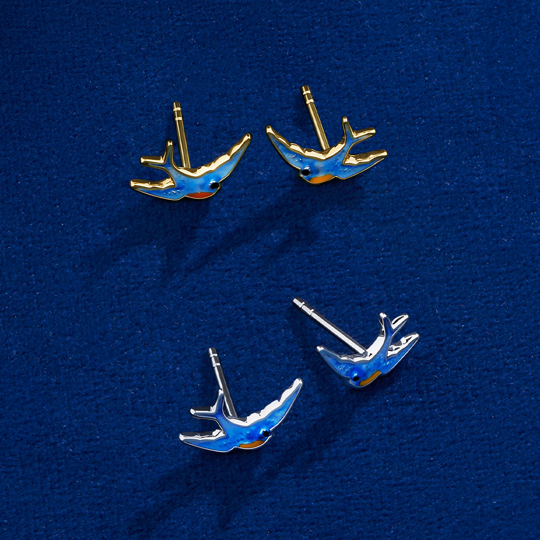 The Wallace Bishop Bluebird of Happiness Stud Earrings in 9ct Yellow Gold, reference 39BB06, measuring 12 x 7.70mm, shown together with the Bluebird of Happiness Stud Earrings in Sterling Silver, reference 49SBB02. Both pairs are bird-shaped studs finished in blue enamel, one in warm yellow gold and one in bright silver.