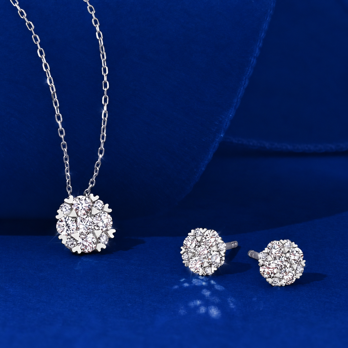 Flat lay view of the Wallace Bishop 0.24 TDW Round Diamond Heart Prong Pendant in 9ct White Gold, reference 3PBB239W, on a cable chain with a parrot clasp, laid flat with the 0.25 TDW Round Diamond Heart Prong Stud Earrings in 9ct White Gold, reference 3EBB239W. The pendant features a cluster of nine claw-set natural round diamonds framed by small heart-shaped prong details, and each earring features a similar cluster of claw-set diamonds.