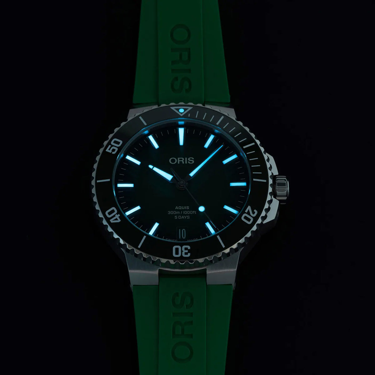 Oris Aquis Date Calibre 400 43.50mm Automatic Watch 01 400 7790 4157-07 4 23 47EB photographed in low light — The Super-LumiNova coating on the baton indices and hands glows clearly in the dark, making the time easy to read underwater or in low-light conditions. The luminous pip on the rotating bezel is also visible, confirming the watch’s dive functionality.