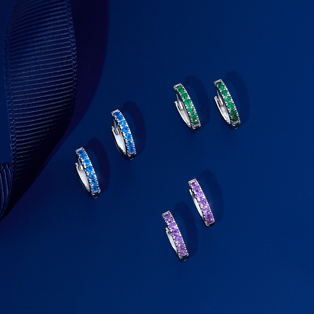 Front-on view of three pairs of Wallace Bishop Cubic Zirconia Huggies in Sterling Silver, each with a 10mm hoop and 1.8mm width: reference 41ECZP88 with a claw-set line of round purple cubic zirconias, reference 41ECZB88 with round blue cubic zirconias, and reference 41ECZG88 with round green cubic zirconias, all in polished sterling silver.