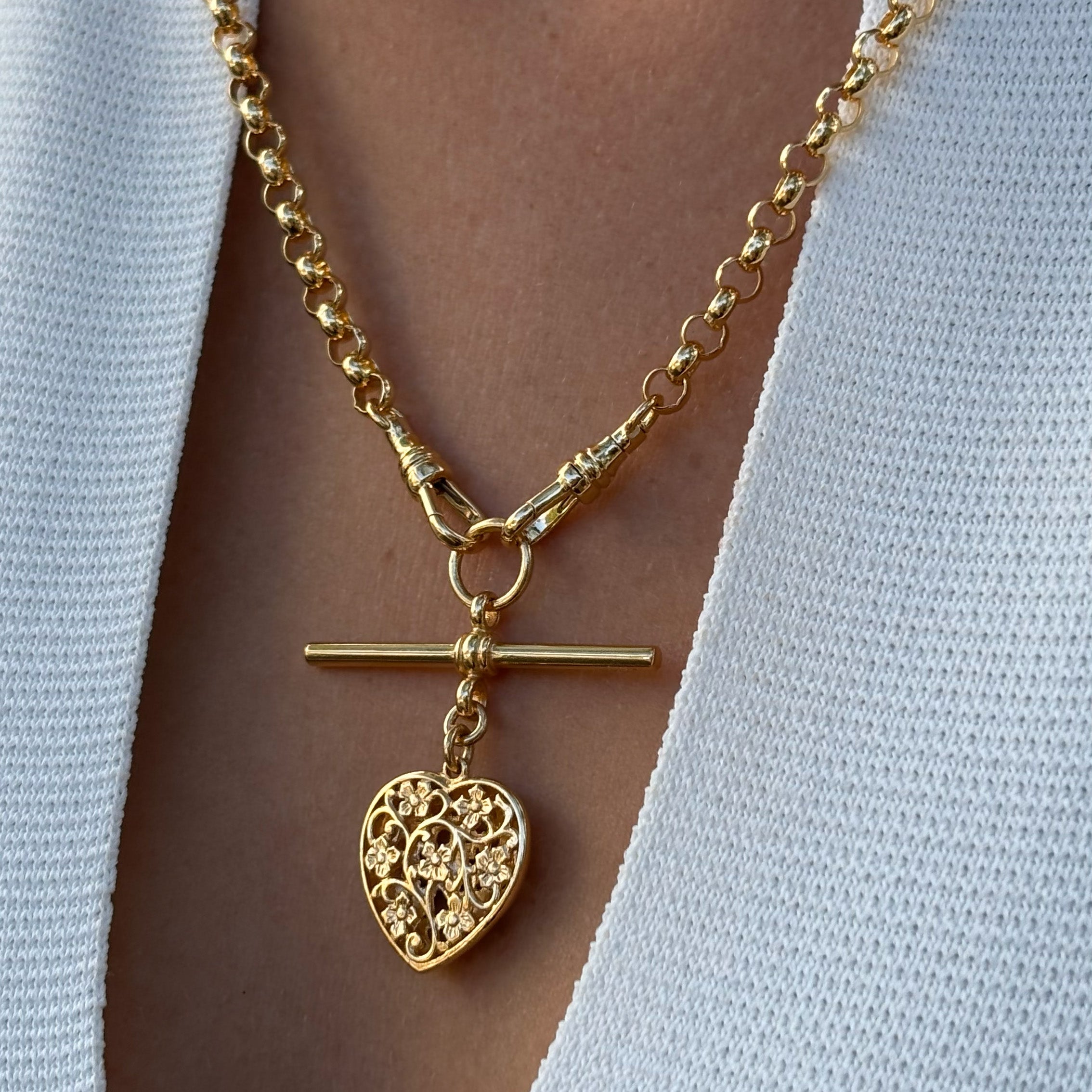 Swivel fob and t bar Gold chain necklace with a detailed heart-shaped pendant on a person