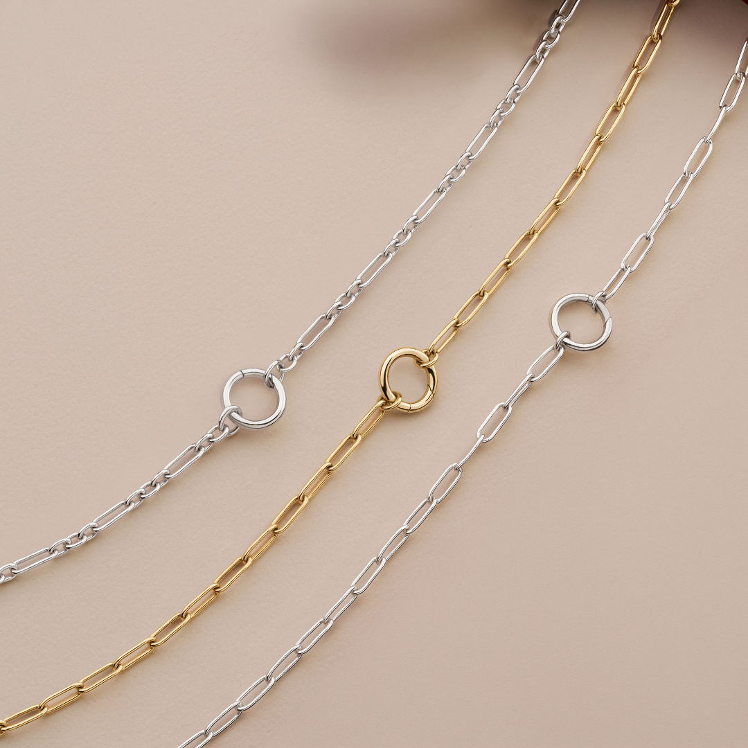 Flat lay view of three Wallace Bishop charm holder chains, each 500mm (approximately 19.7 inches) in length and 2.8mm in width, with a parrot clasp: the Paperclip Charm Holder Chain in Sterling Silver, reference 44PCCH01, the Trombone Link Charm Holder Chain in Sterling Silver, reference 44TBCH01, with a round ring for charms and pendants, and the Paperclip Charm Holder Chain in 9ct Yellow Gold, reference 46PCCH01Y.