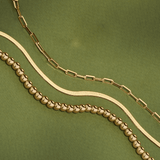 Close-up of a 9ct yellow gold herringbone bracelet showcasing polished flat links with other stackable gold bracelets