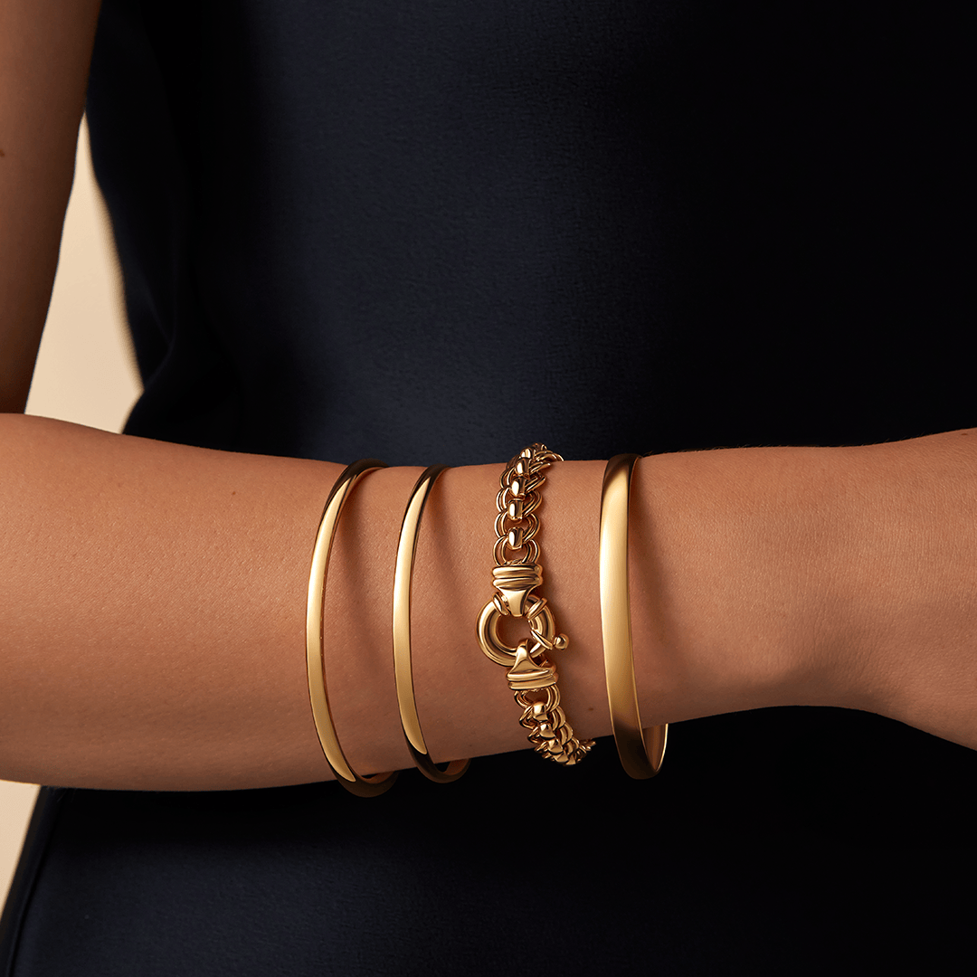 Solid round bangle in 9ct yellow gold featuring a classic polished design with a 4mm width and 65mm size displayed with three other gold bracelets