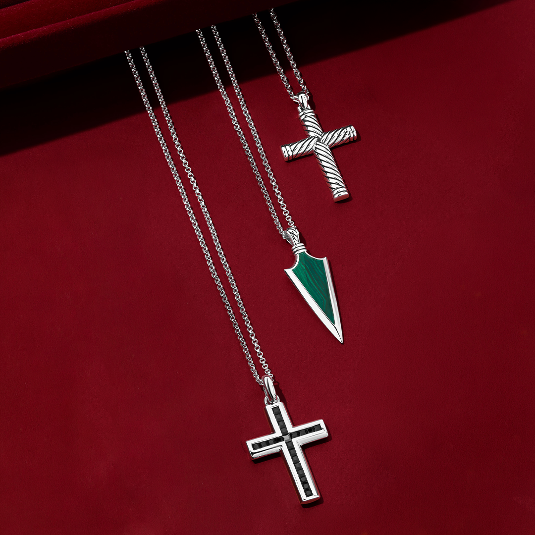 Front-on view of three Wallace Bishop gents pendants in sterling silver, each on a 650mm (approximately 25.6 inch) chain: the Cross Gents Pendant, reference 49NRP002, 41.50mm in length, with a rope design and a polished finish and a parrot clasp, , 47.20mm in length, with a polished face and a rope detail around the edge and a parrot clasp, the Malachite Arrowhead Gents Pendant, reference 4UNKMLSS1, 14.60mm in length, with a natural green malachite in an arrowhead