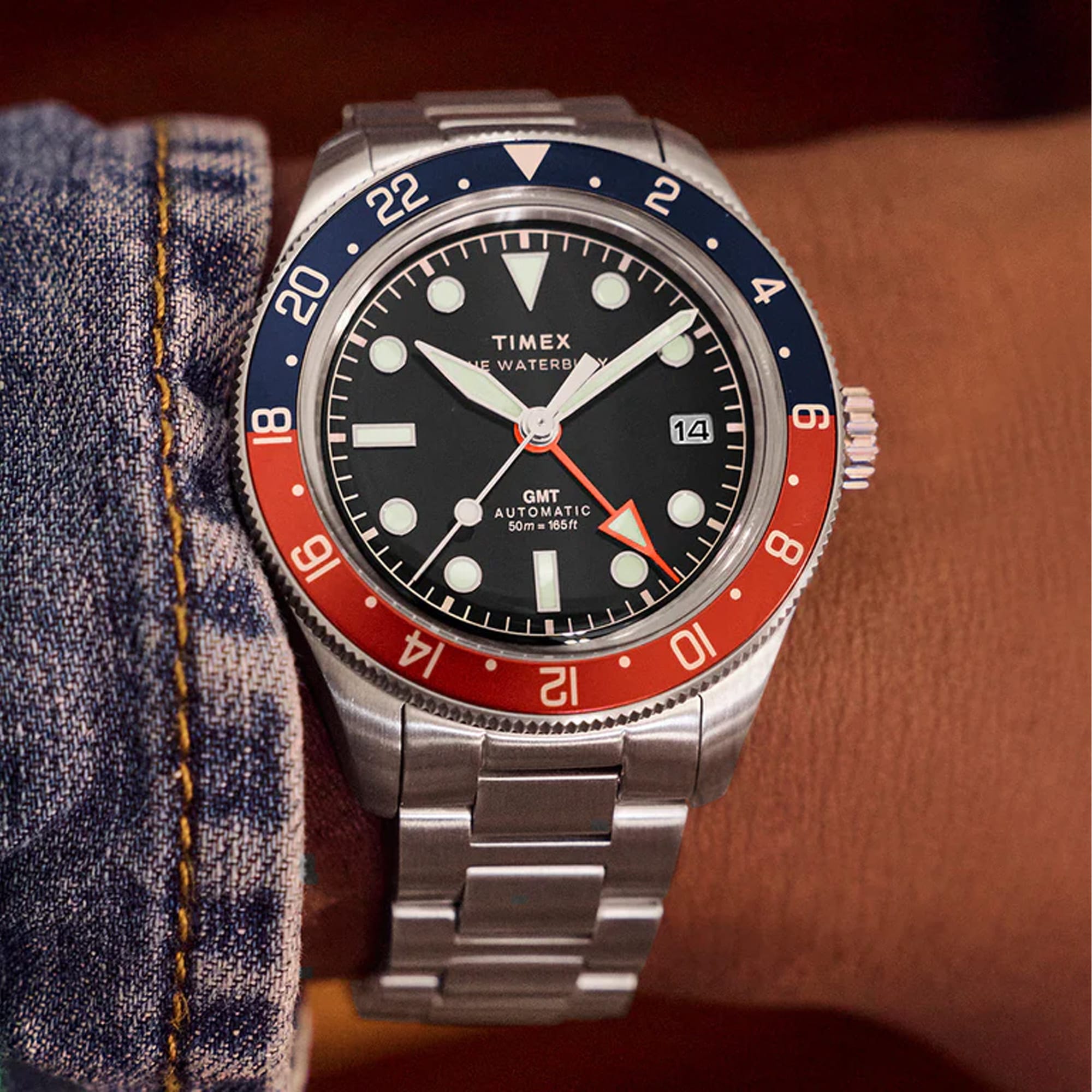 Timex Waterbury Heritage Automatic GMT men’s watch with black dial, stainless steel bracelet, and stainless steel case featuring a rotating bezel and GMT hand for dual time zone tracking in a classic heritage design.