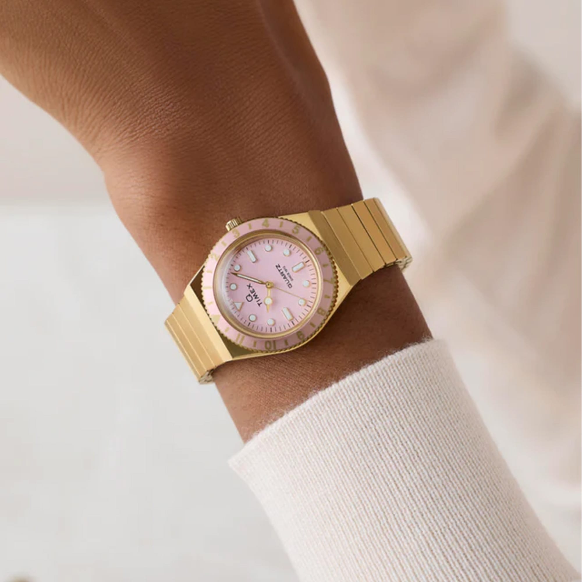 Gold-tone Timex Q Mini women’s watch with a pastel pink analog dial, luminous markers, 30mm stainless steel case, and matching expansion bracelet inspired by vintage 1970s styling - on wrist