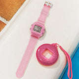The Casio Baby-G BGD10KG-4D centre case removed from the bezel and inserted into the included customisable silicone holder with acrylic panels — shown as a bag charm or waist accessory with the rotating pixel-art animations visible on the LCD display.