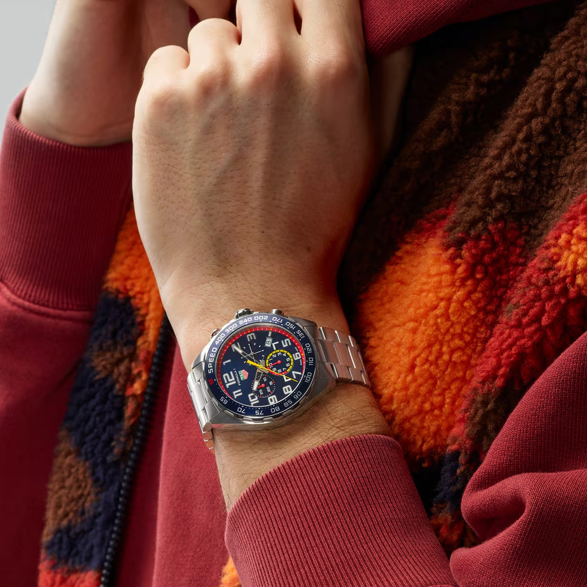 TAG Heuer Formula 1 Chronograph x Red Bull Racing CAZ101AL.BA0842 shown worn on the wrist, illustrating the case proportions and steel bracelet fit. The blue dial and red accents stand out against the sleeve in frame.