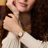 Lifestyle image of the Daniel Wellington Corta Grain-Link Women’s 24mm Quartz Watch DW00100993 styled with gold jewellery. The warm gold tone layers easily with gold bracelets and rings.