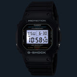 Casio G-Shock DW5600UE-1D front view — all-black square matte resin case, rectangular five-line LCD display. Images shows the blacklight in a dark background