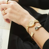 The EM1202-50P worn on the wrist, highlighting its sculpted 26mm by 31mm pear-shaped case. The integrated gold-tone bracelet follows the case contours for a seamless fit.