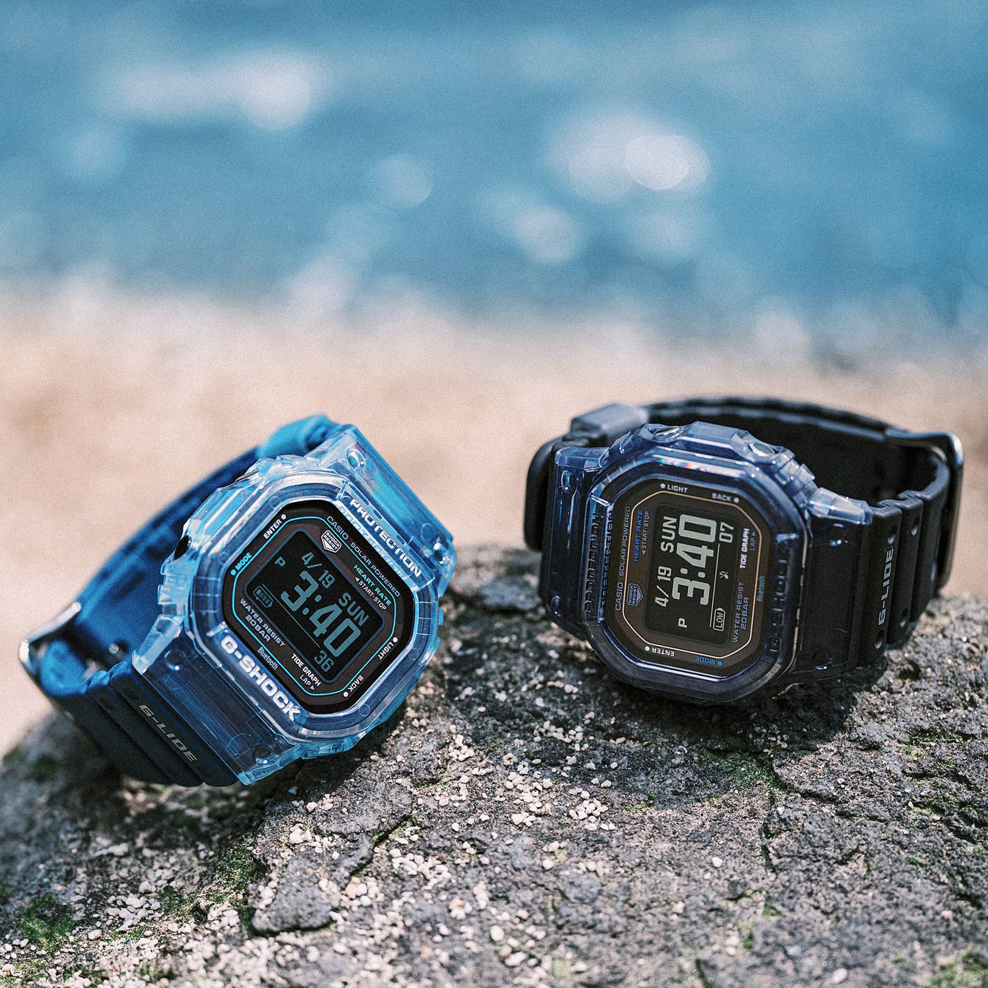 Two Casio G-LIDE GBXH5600-1D Black Digital Watches resting on a rocky surface in an outdoor environment. Rugged square case construction with black resin strap and multi-function digital dial on display.