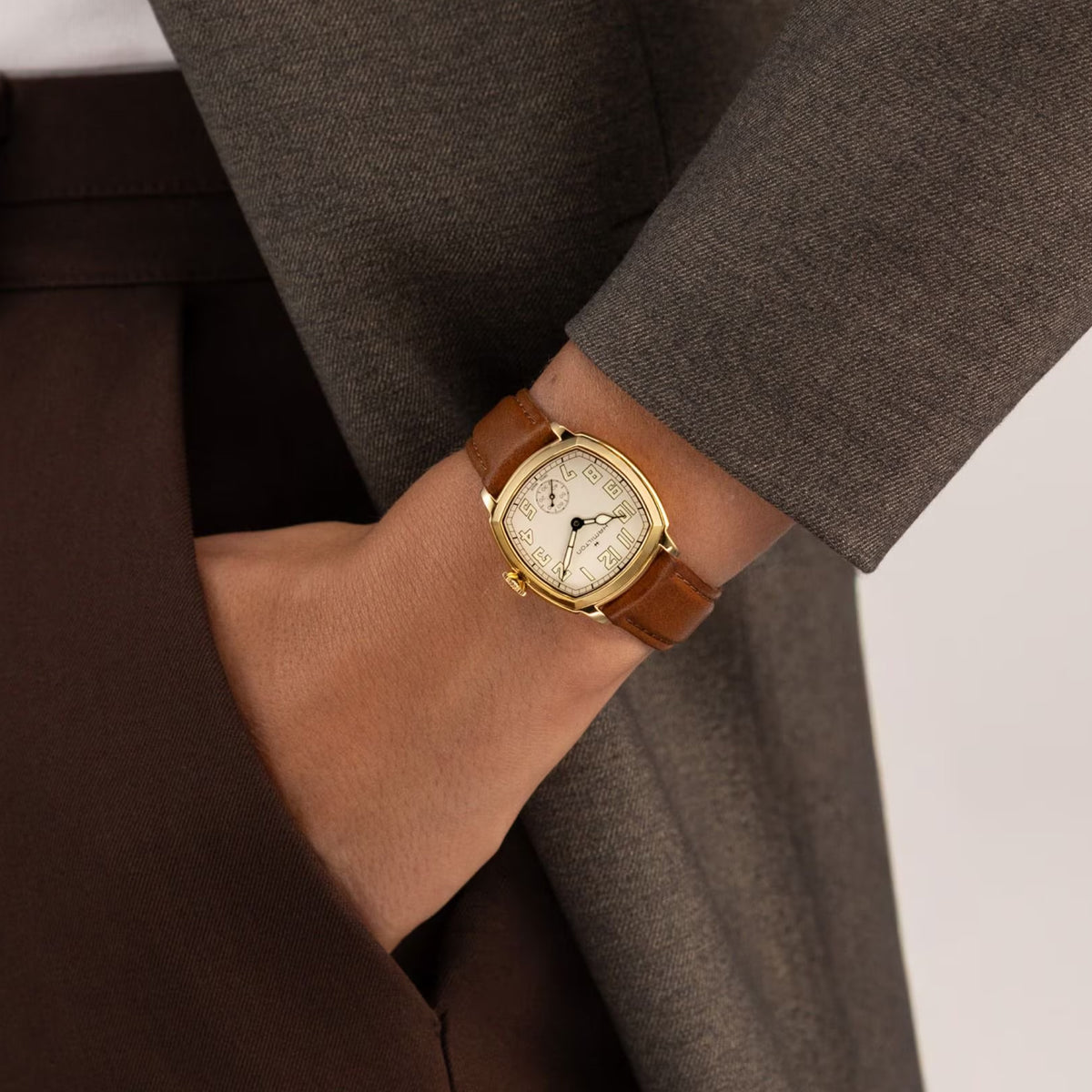 Hamilton American Classic Cushion Mechanical Women’s 30mm Watch H36119520 is worn on the wrist with its brown leather strap fastened. The compact 30mm case and beige dial suit a classic dress watch look.