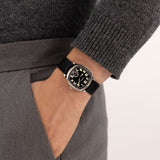 Hamilton American Classic Cushion Mechanical Unisex 34mm Watch H36129730 is worn on the wrist with its black leather strap fastened. The square case and black dial suit a classic dress watch look.