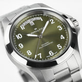 Close-up of Hamilton Khaki Field King H64475160 green sunray dial showing bold Arabic numerals, luminous syringe hands, and curved day-date window at 12 o'clock