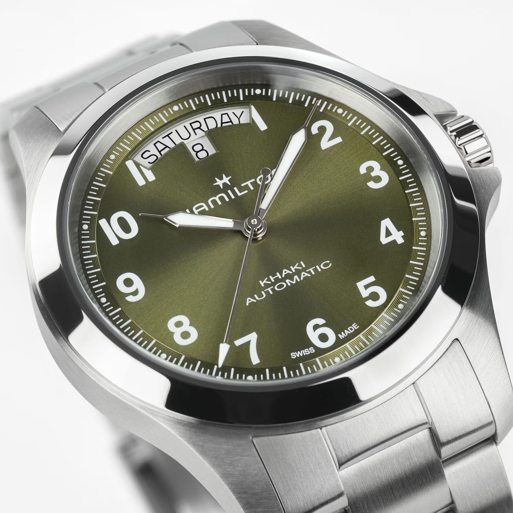 Close-up of Hamilton Khaki Field King H64475160 green sunray dial showing bold Arabic numerals, luminous syringe hands, and curved day-date window at 12 o'clock