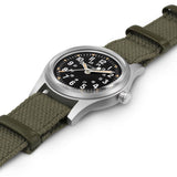 Hamilton Khaki Field Mechanical 36mm Watch H69399930 is shown at a 3/4 angle, highlighting the acrylic box glass, black dial, and khaki NATO strap together. The angle showcases the watch's rugged, purpose-built military design produced exclusively throughout 2026.