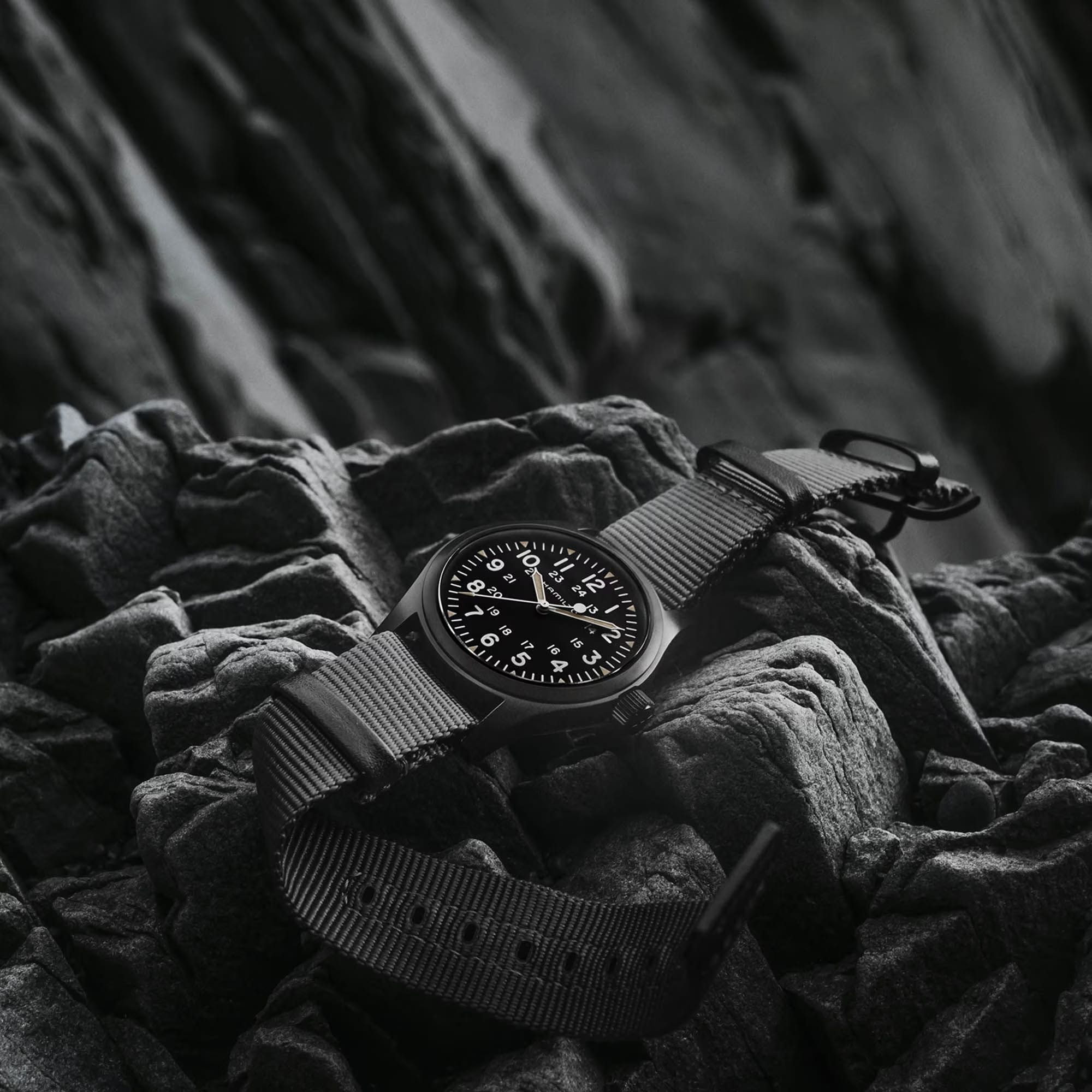 Hamilton Khaki Field Mechanical 38mm Watch H69409930 is shown at a 3/4 angle, highlighting the sapphire crystal, black dial, and NATO strap together. The angle showcases the watch's faithful recreation of its 1960s military field watch origins.