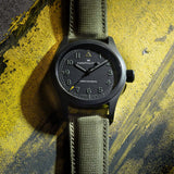 Hamilton x Call of Duty Khaki Field Mechanical Men’s 38mm Watch H69469930 is shown in close up, revealing the textured black dial, white Arabic numerals and subtle railroad minute track. The yellow triangle at 12 o’clock matches the yellow tip of the seconds hand.