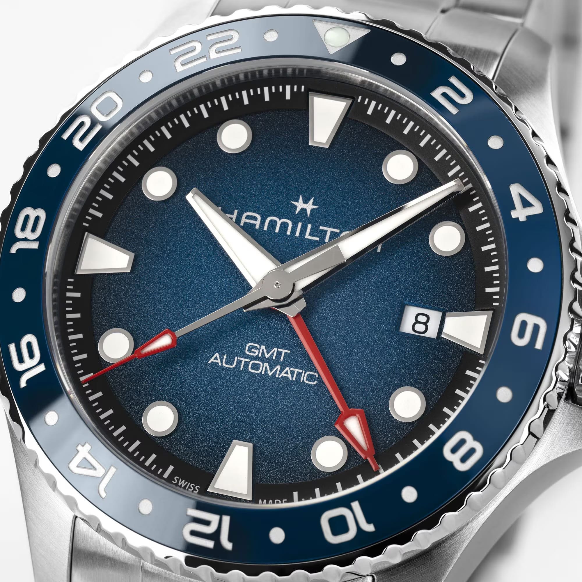 Hamilton Khaki Navy Scuba Auto GMT 43mm Watch H82535140 is shown at a 3/4 angle, highlighting the sapphire crystal, blue dial, and ceramic GMT bezel together. The angle showcases the watch's travel-ready, diving-inspired design.