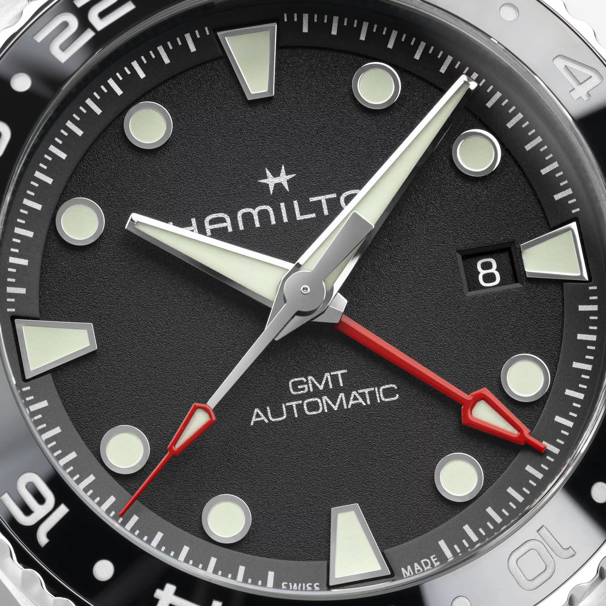 Hamilton Khaki Navy Scuba Auto GMT 43mm Watch H82555330 is shown at a 3/4 angle, highlighting the sapphire crystal, black dial, and ceramic GMT bezel together. The angle showcases the watch's travel-ready, diving-inspired design.