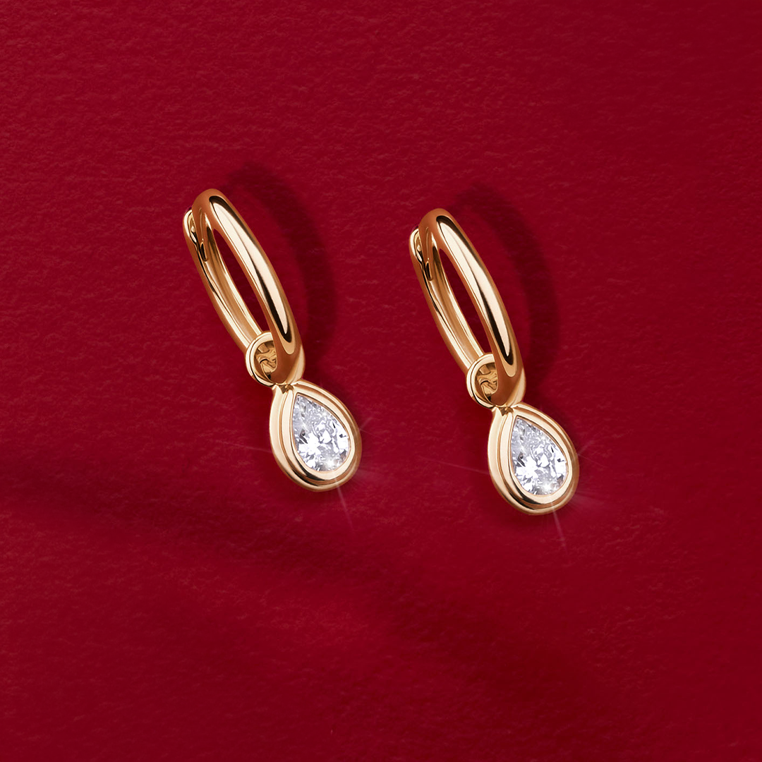 Flat lay view of the Wallace Bishop 0.30 TDW Pear-Cut Lab-Grown Diamond Double Bezel Drop Earrings in 9ct Yellow Gold, reference LGHUGP30, measuring 19mm in length, laid flat. Each earring features a single pear-cut lab-grown diamond in a double bezel setting.