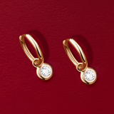 Flat lay view of the Wallace Bishop 0.30 TDW Round Lab-Grown Diamond Double Bezel Drop Earrings in 9ct Yellow Gold, reference LGHUGR30, measuring 19mm in length, laid flat. Each earring is a huggie with a single round brilliant cut lab-grown diamond in a bezel set drop.