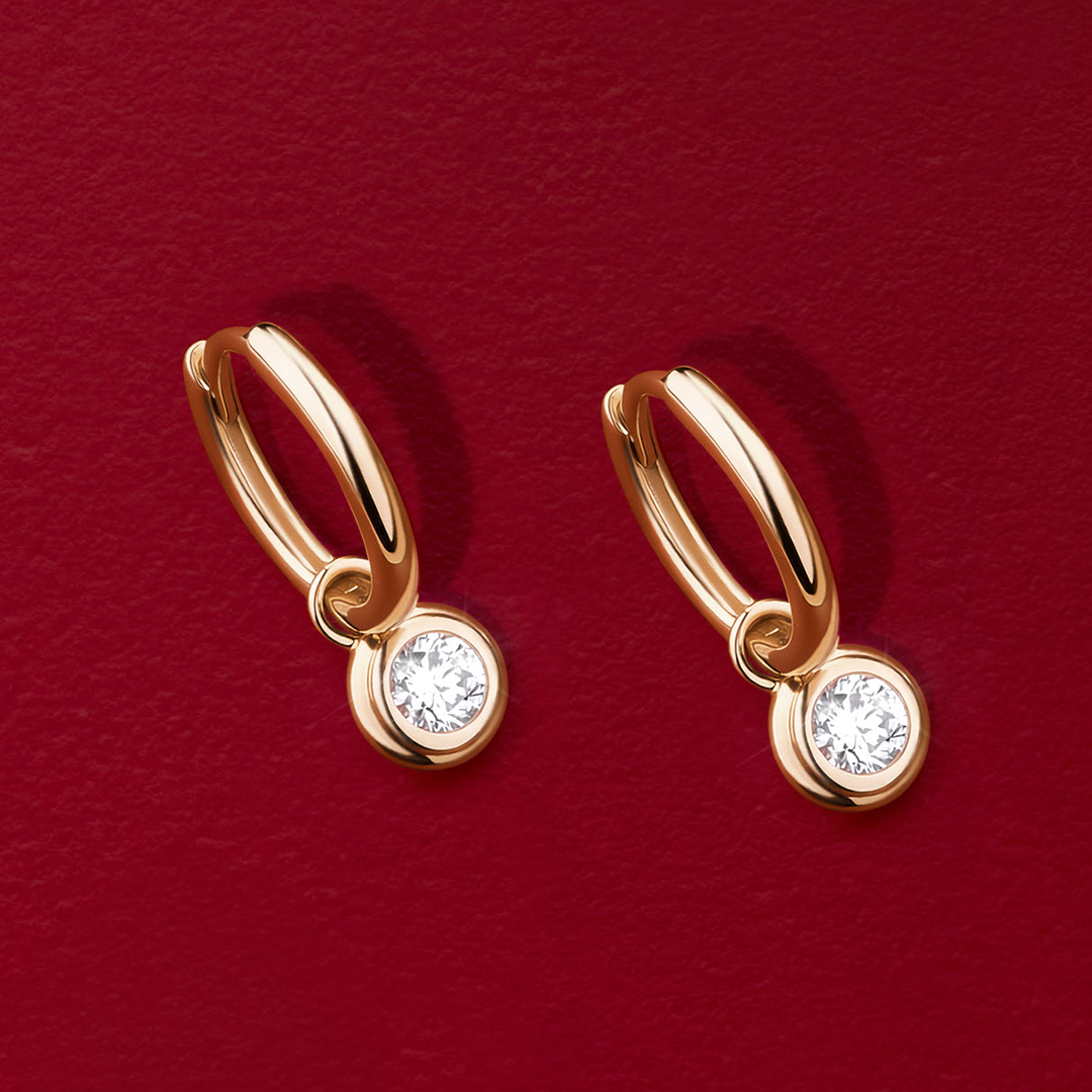 Flat lay view of the Wallace Bishop 0.30 TDW Round Lab-Grown Diamond Double Bezel Drop Earrings in 9ct Yellow Gold, reference LGHUGR30, measuring 19mm in length, laid flat. Each earring is a huggie with a single round brilliant cut lab-grown diamond in a bezel set drop.