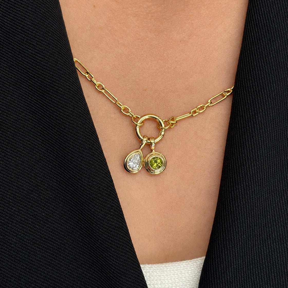 On-body view of a neck wearing two Wallace Bishop Double Bezel Pendants in 9ct Yellow Gold: the 0.30 TDW Pear-Cut Lab-Grown Diamond Double Bezel Pendant, reference LGNDBP30, and the Round Peridot Double Bezel Pendant, reference 93PDRDPE1Y, with the pear-cut diamond and the round green peridot each set in a polished gold double bezel.