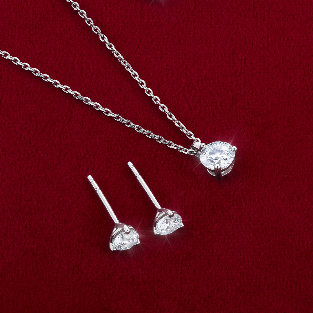 Flat lay view of the Wallace Bishop 0.50 TDW Round Lab-Grown Diamond Solitaire Pendant in Sterling Silver, reference LGPDSS050, on a 500mm (approximately 19.7 inch) fine cable chain, laid flat with the Round Lab-Grown Diamond Solitaire Stud Earrings in Sterling Silver, reference LGERSS050. Each piece features a round lab-grown diamond in a three-claw setting.