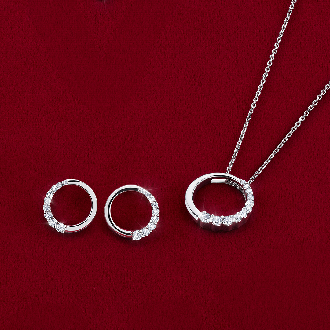 Flat lay view of the Wallace Bishop 0.40 TDW Round Lab-Grown Diamond Circle Pendant & Earrings Set in Sterling Silver, reference LGSETRNDSS, with the pendant on a 500mm (approximately 19.7 inch) chain laid flat beside the stud earrings, which have butterfly backs. Each circle is set with round lab-grown diamonds around half of its edge.