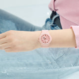 Casio Baby-G+PLUS BGA15K-4A front view — pastel pink matte round resin case, shimmering metal dial, Arabic numerals, three-hand analogue display with rotating day design.