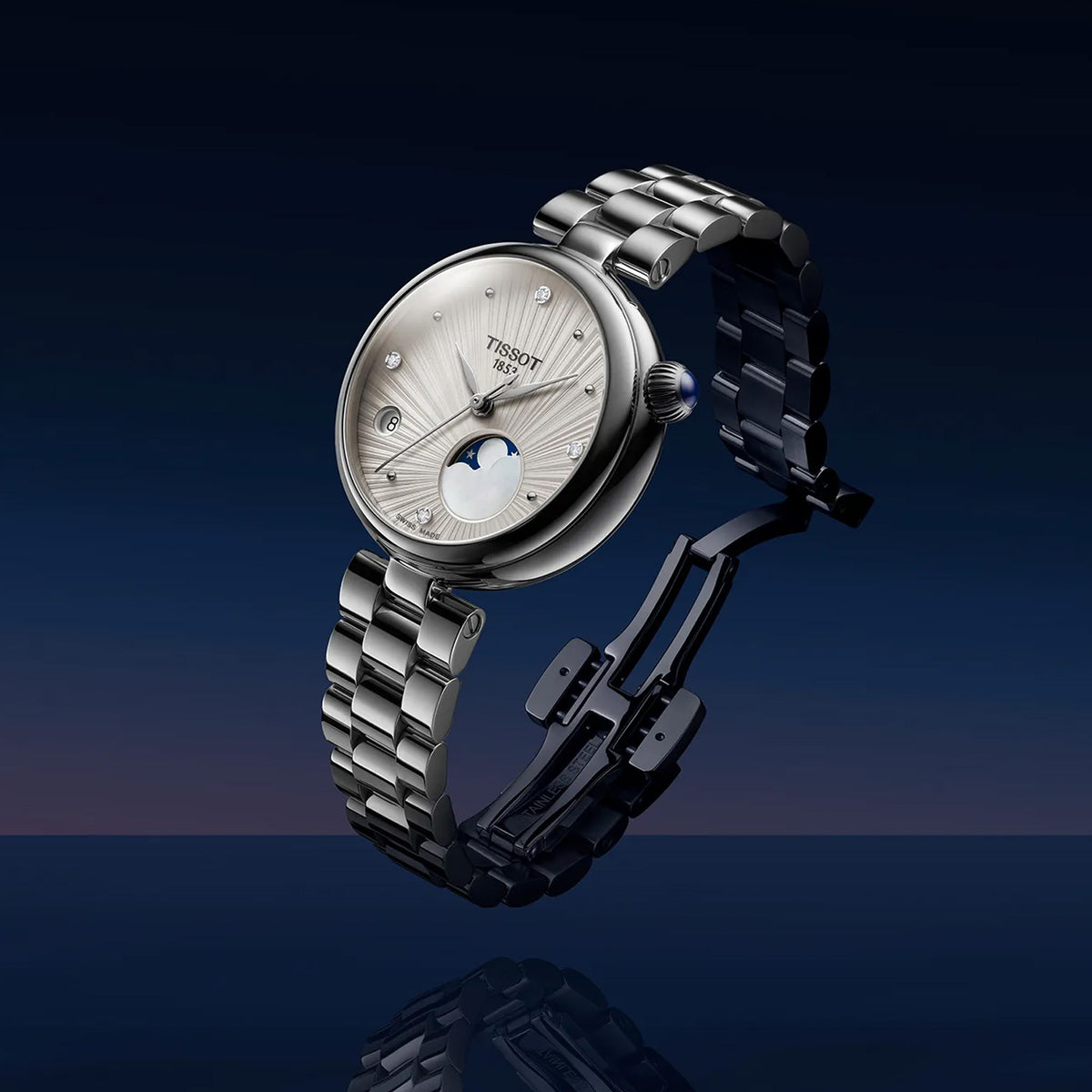 A Tissot watch with a silver-toned metal bracelet and a white sunburst dial featuring a moonphase indicator, shown floating against a dark blue gradient background.