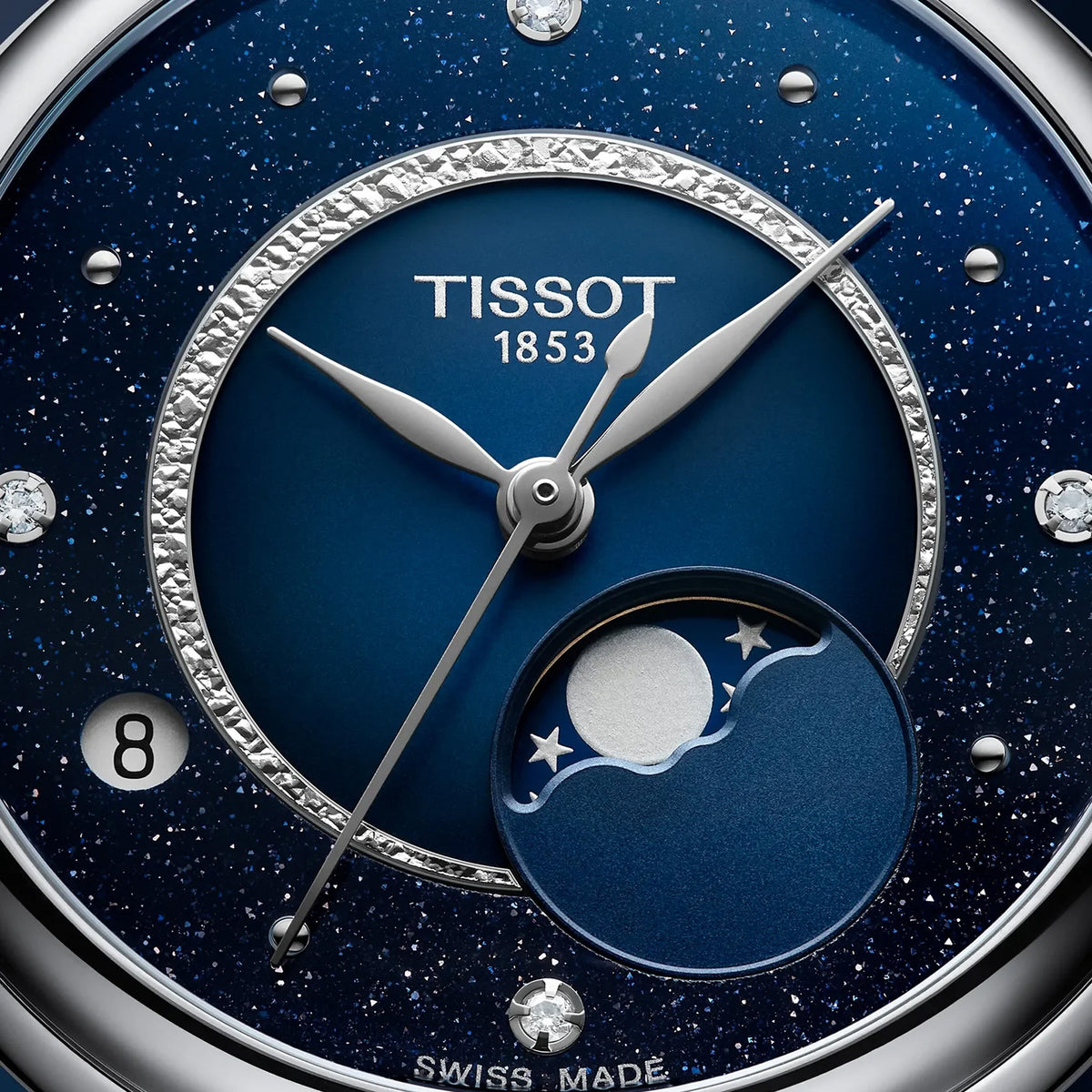 Close-up of a Tissot watch dial with a deep blue speckled starfield finish, silver hands and markers, a crystal-rimmed inner ring, and a moonphase subdial at the lower right.