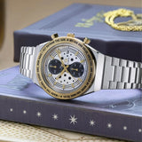 The Timex x Harry Potter Time Turner Quartz Chronograph 40mm Watch TW2Y75900 is shown beside a gold Time-Turner pendant, with its hands and hour markers glowing in dim light. The star-patterned dial and silver-tone bracelet suit Harry Potter fans and collectors.