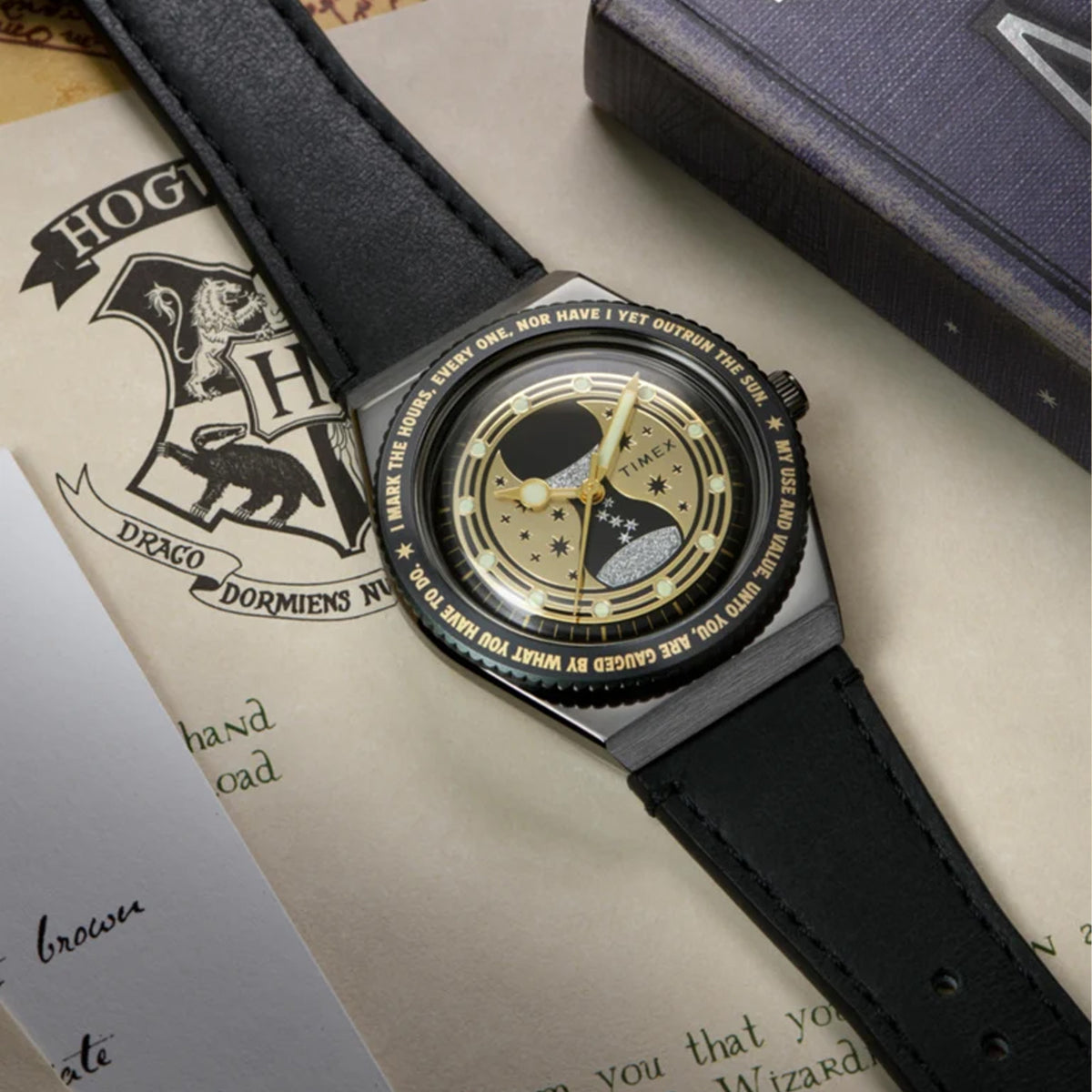 The Timex x Harry Potter Time Turner Quartz 36mm Watch TW2Y76000 is shown beside a gold Time-Turner pendant and Hogwarts-themed papers. The black strap and gold hourglass dial suit Harry Potter fans and collectors.