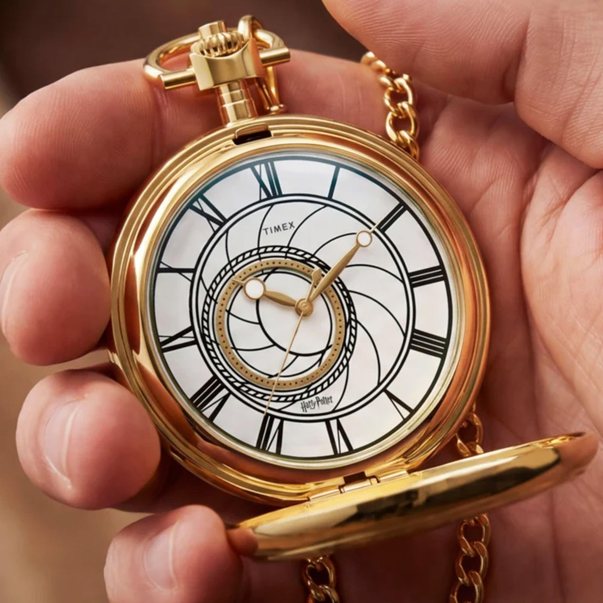The Timex x Harry Potter Time Turner 48.5mm Pocket Watch TW2Y99600 is shown open beside a burgundy and gold Gryffindor scarf. The gold-tone case and white dial suit Harry Potter fans and collectors.