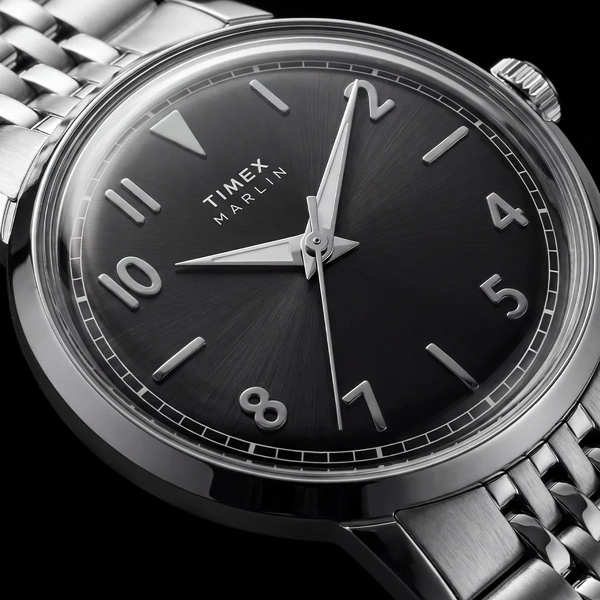 Close-up of a Timex Marlin wristwatch with a black dial, silver-tone stainless steel case, and matching metal link bracelet on a dark background.