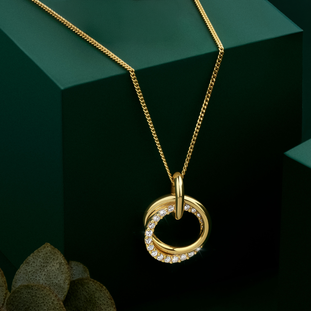 Flat lay view of the Wallace Bishop Cubic Zirconia Circles Pendant in 9ct Yellow Gold, reference 68PCZ500, measuring 16.8mm by 11.25mm, laid flat. The pendant features two interlocking circles, one in plain polished gold and one set with round cubic zirconias.