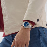 TAG Heuer Formula 1 Date WAZ1118.BA0875 shown worn on the wrist, illustrating the case proportions and steel bracelet fit. The blue dial stands out against the sleeve in frame.