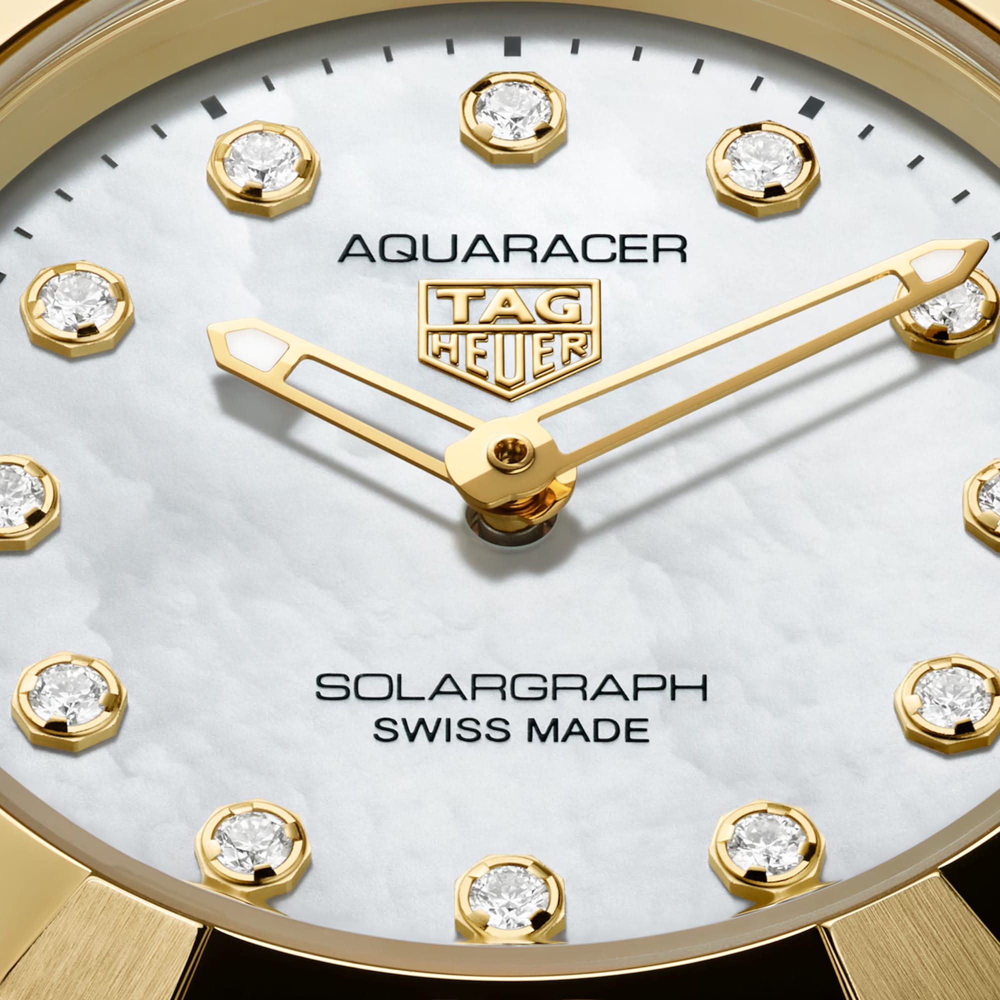 TAG Heuer Aquaracer Professional 100 Solargraph WBP1420.BB0006 captured in extreme close-up on the white mother-of-pearl dial, highlighting the dodecagonal diamond hour markers and gold-plated hands. The Super-LumiNova-filled hands sit against the pearlescent dial surface.