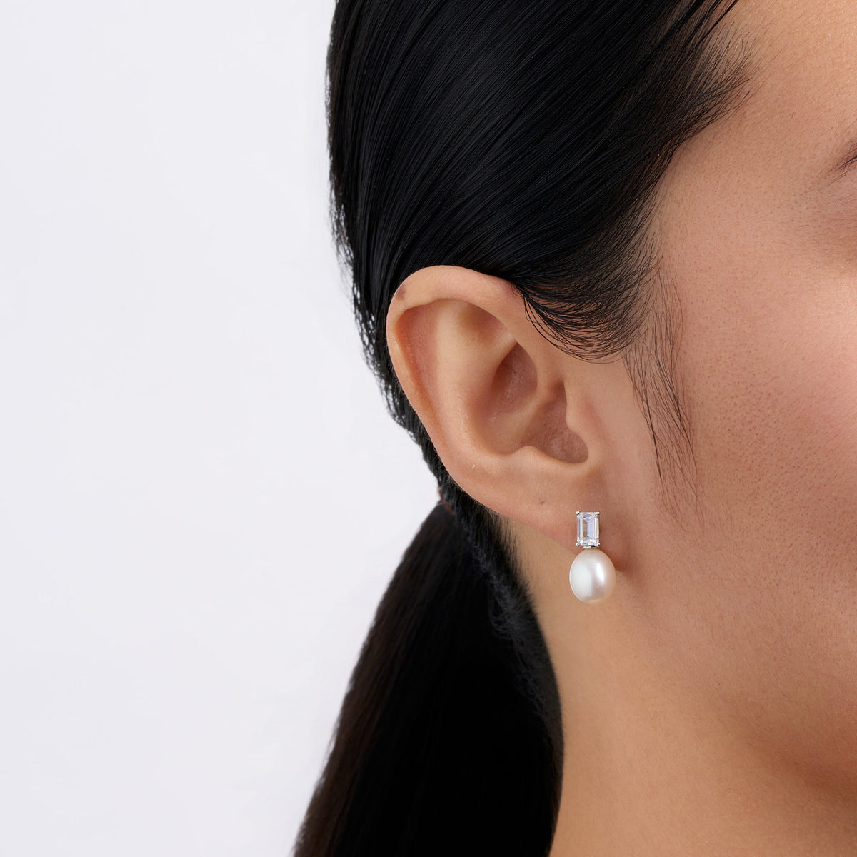 On-body view of a model wearing the Wallace Bishop Freshwater Pearl & Cubic Zirconia Drop Earrings in Sterling Silver, with white rice shaped pearls hanging below the emerald cut cubic zirconia.