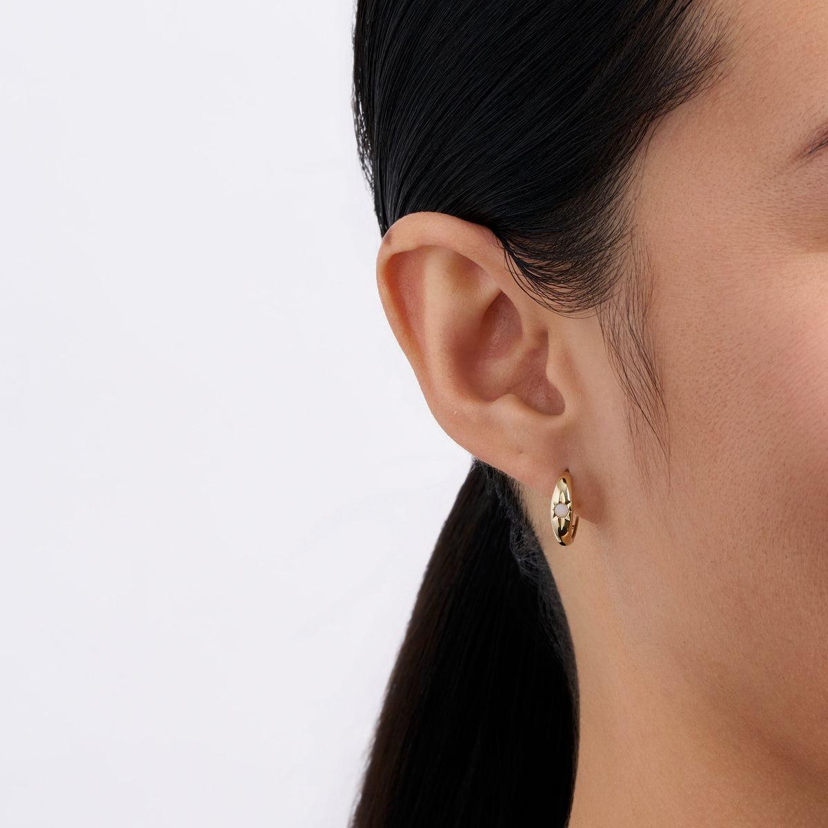 On-body view of a model wearing the Wallace Bishop Opal Starburst Huggies in 9ct Yellow Gold, hugging the earlobe with a 2.5mm round white opal on each earring.